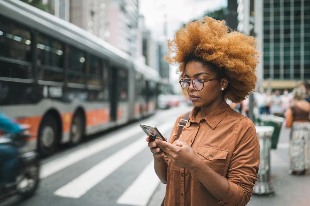 Mulher consultando o celular em ponto de ônibus